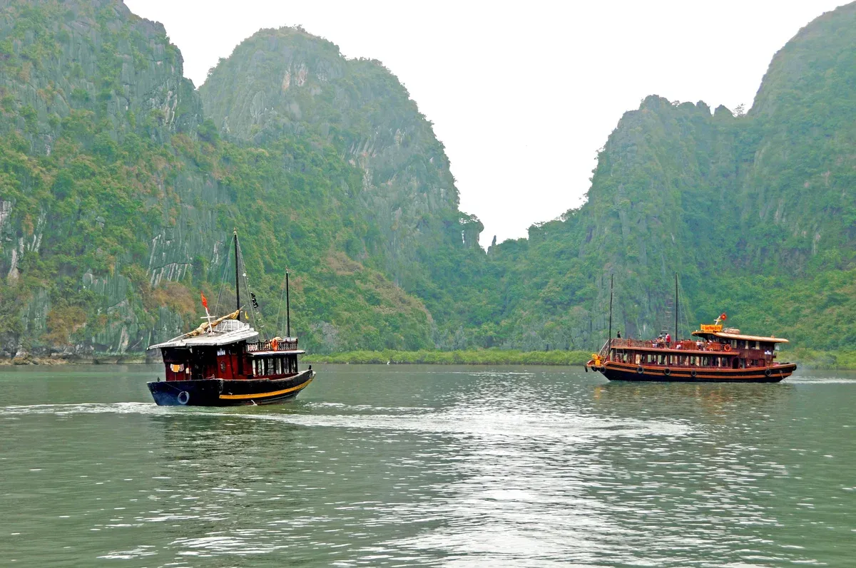 Two tour boats cruising between karsts on a Ha Long Bay junk boat cruise