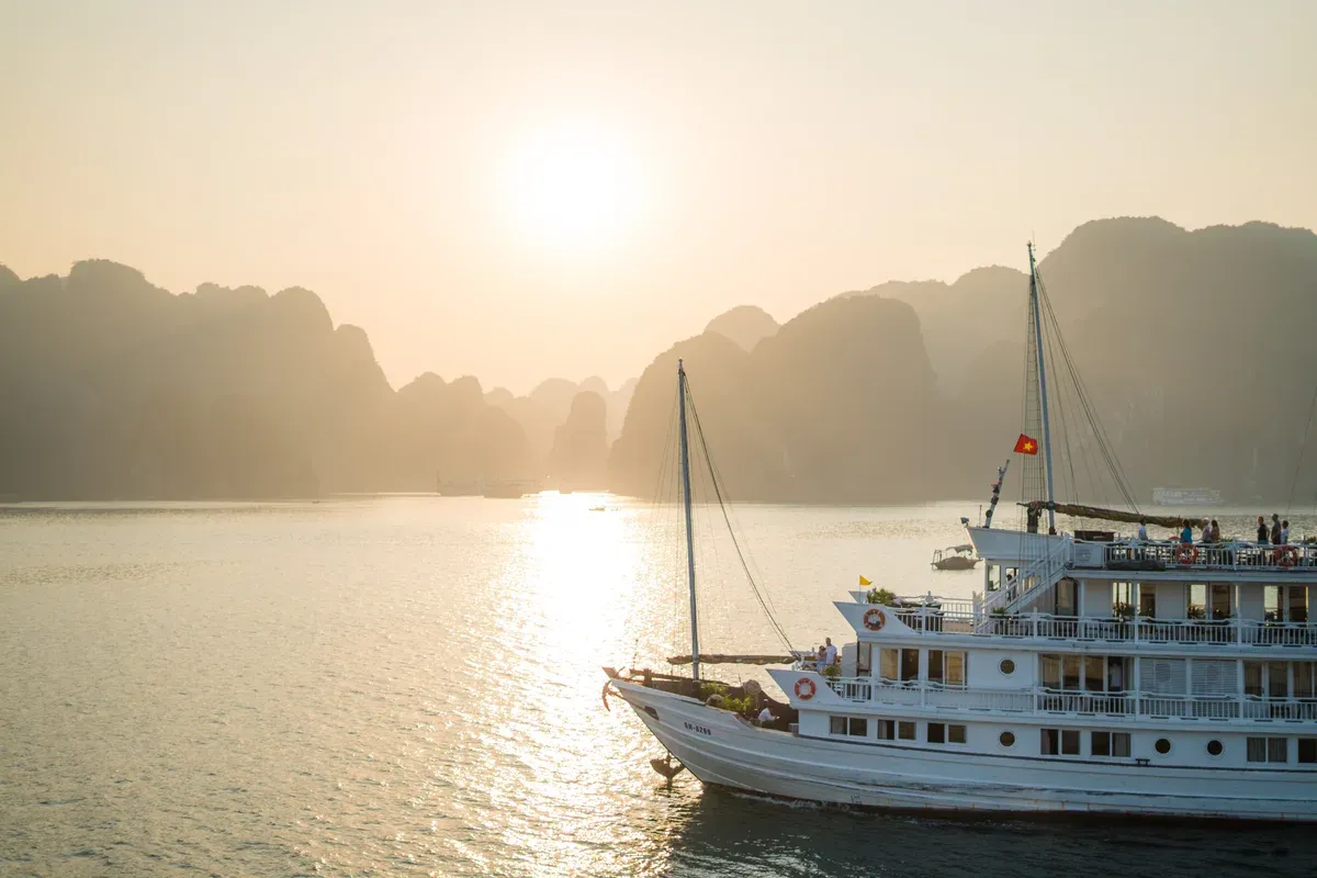 Sail-rigged cruise boat in warm sunset light among karsts on a Ha Long Bay junk boat cruise