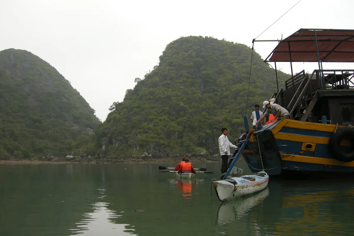 Cruise tender and kayaks at the foot of green karsts on a Ha Long Bay junk boat cruise